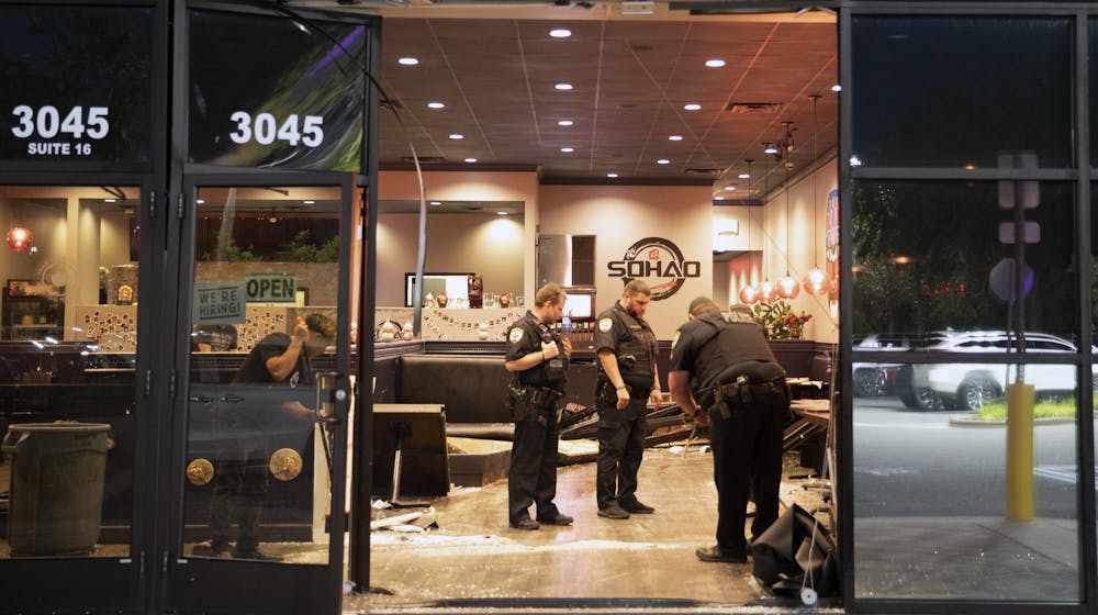 Police officers investigate the area and help clean broken glass from the floor of SOHAO Cafe & Gator Suyaki after a blue Dodge was driven through the front of the restaurant on Monday, May 17, 2021.