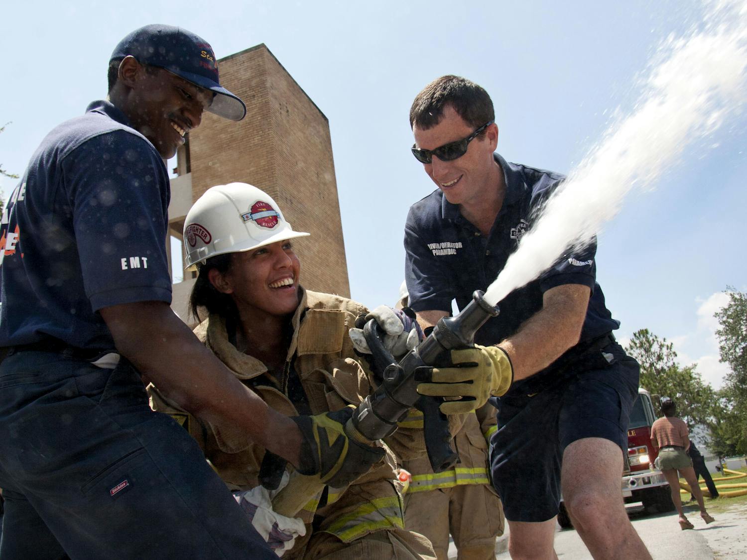 CITIZENS' FIRE ACADEMY -- Reggie Kinsey, 24, an EMT at Station 7, and Greg Fenn, 32, a driver/operator at Station 1, assist Mary Ann Dematas, 30, with a 1 1/4 inch (diameter) fire hose, spraying 170 gallons of water per minute, Saturday at Station 3, near Waldo Road and 8th Avenue. Dematas, who works in the Lawn and Gardening Department at Home Depot, tried to compare the water pressure to a difficult task, but carrying 30-pound bags of soil doesn't illustrate the constant force her body stood against.