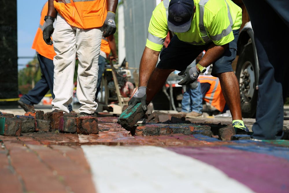 A City of Gainesville Public Works employee removes a green brick from the  rainbow crosswalk on Northeast First Street to make room for new gray bricks on Monday, August 25, 2025.