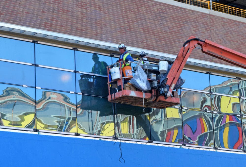 Construction workers fix window treatments on the new building of UF Health Shands Hospital on Wednesday. The children's hospital, across Archer Road, is reflected in the windows.