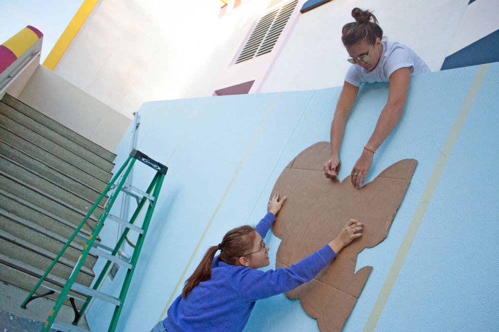 Kate Keskinen, a 27-year-old Santa Fe College employee, helps Jovana Christiani trace the design for Santa Fe’s new mural Tuesday. They helped a Dublin-based urban artist paint the mural.
