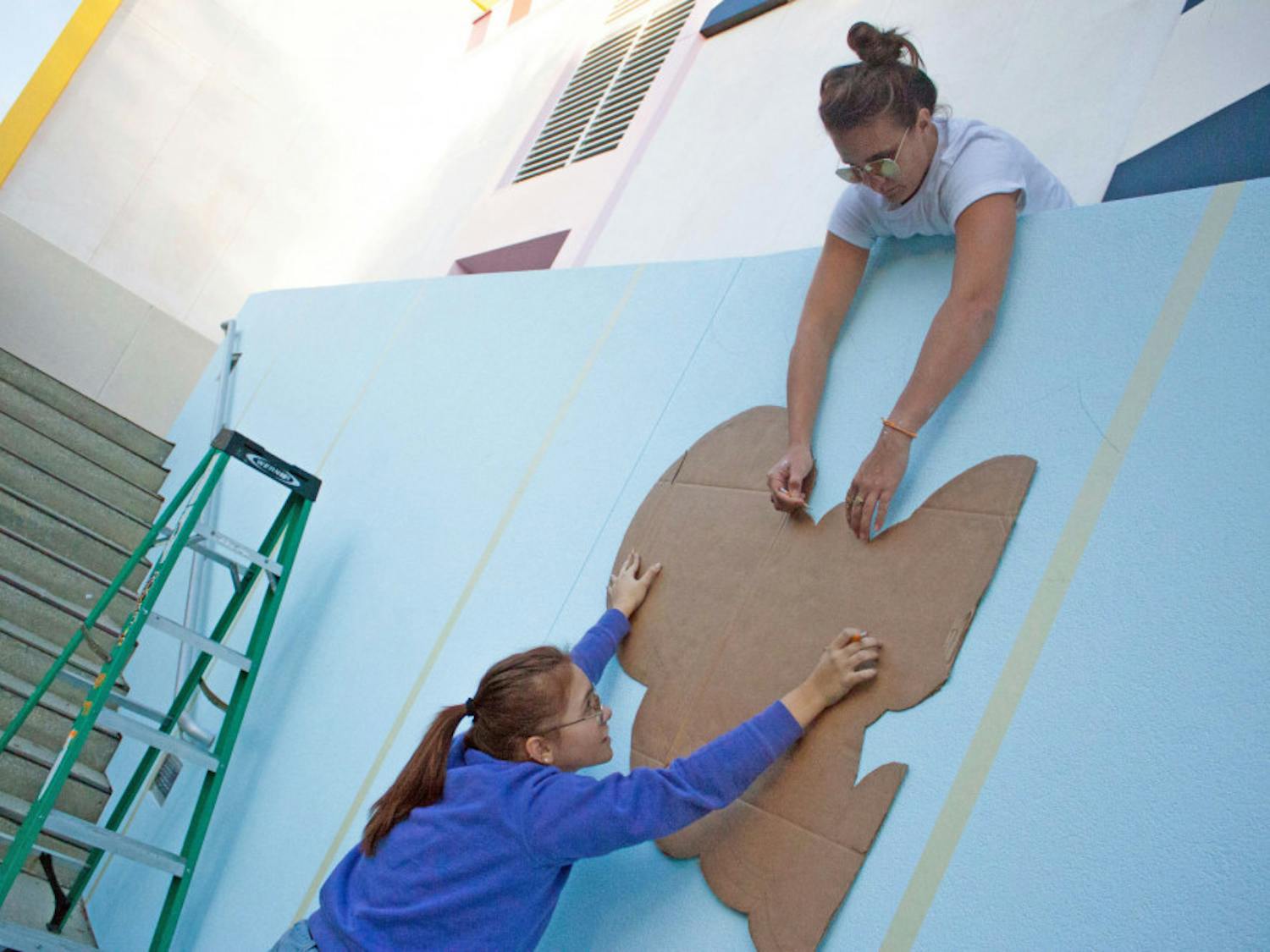 Kate Keskinen, a 27-year-old Santa Fe College employee, helps Jovana Christiani trace the design for Santa Fe’s new mural Tuesday. They helped a Dublin-based urban artist paint the mural.