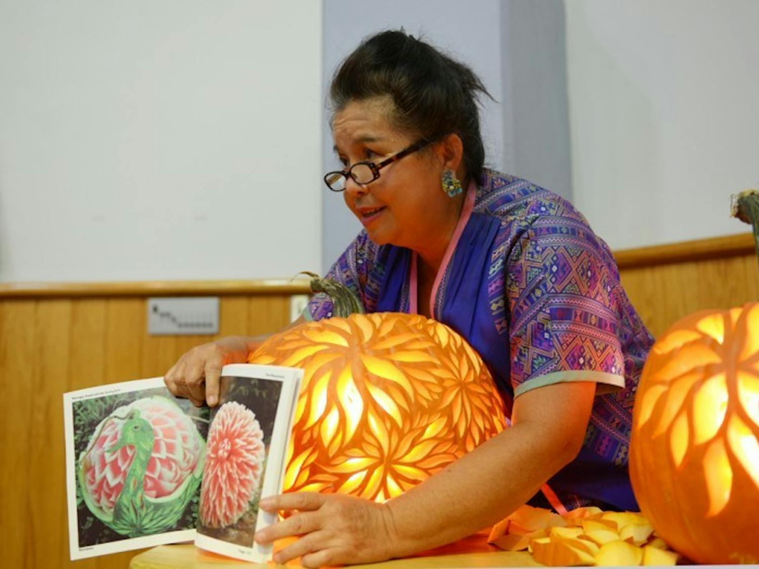 Kae-Sa-Luk Master Pam Maneeratana, 60, shows off her book, 'Messages Found with the Carving Knife', during a carving demonstration at the Alachua County Headquarters Library on Saturday. Maneeratana was trained by an instructor from the Royal Palace in Thailand as a child and has been carving professionally for over 30 years.