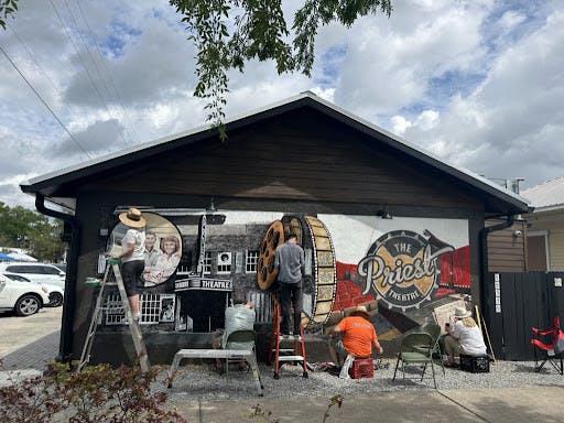 Muralists paint a mural of The Priest Theatre in High Springs on Saturday, March 25, 2023.
