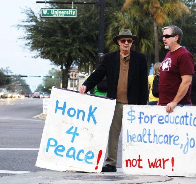 Gainesville residents Arnie Lapidus, 79, left; and Greg Mullaley, 59, right; stand on the southeast corner of West University Avenue and Southwest 13th Street on Tuesday afternoon. The men stood on the corner with about six other people to support bringing troops back to the United States and limiting military spending.
