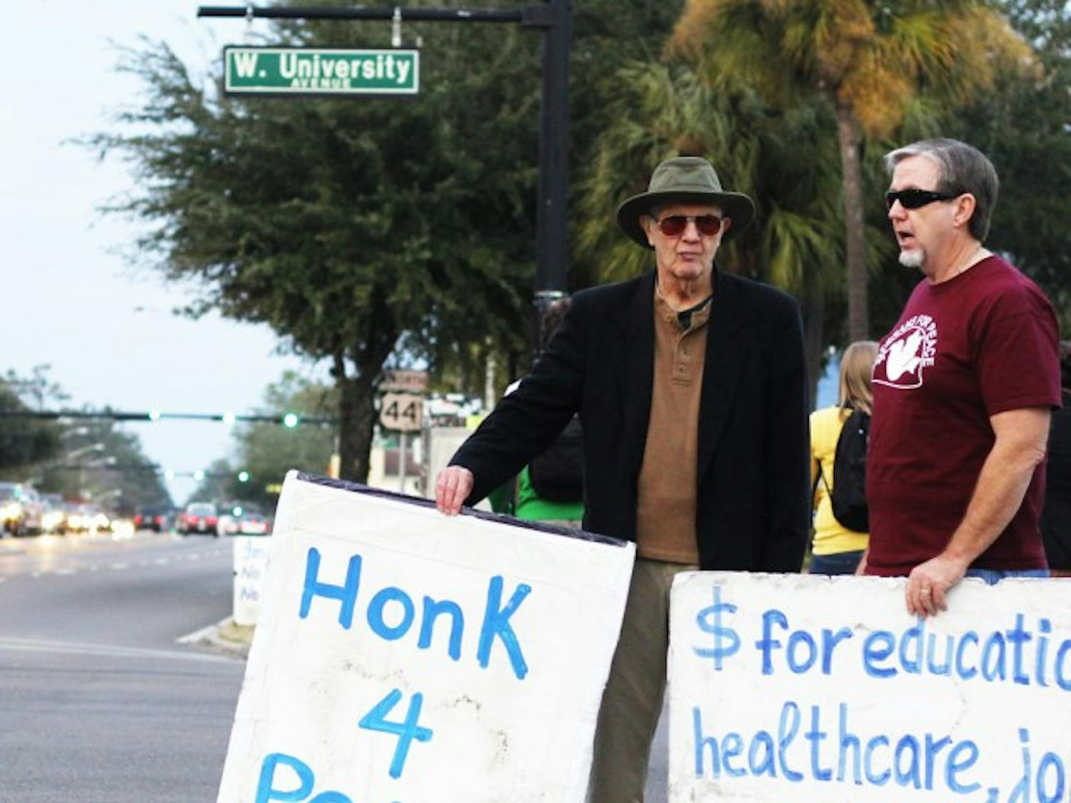Gainesville residents Arnie Lapidus, 79, left; and Greg Mullaley, 59, right; stand on the southeast corner of West University Avenue and Southwest 13th Street on Tuesday afternoon. The men stood on the corner with about six other people to support bringing troops back to the United States and limiting military spending.