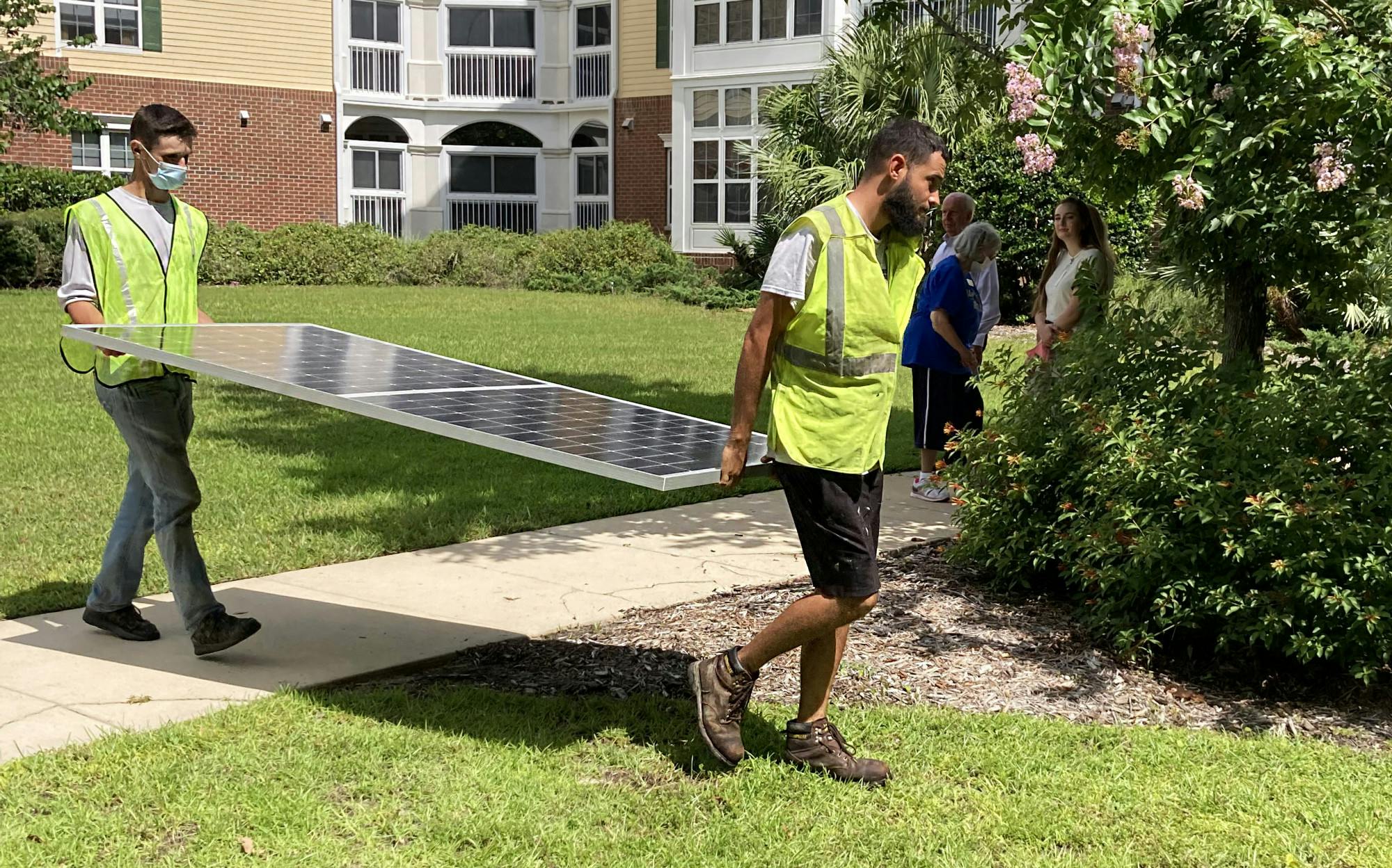 Workers lift up the first solar panel installed on the rooftops of Oak Hammock at the University of Florida on Tuesday, July 20, 2021. 