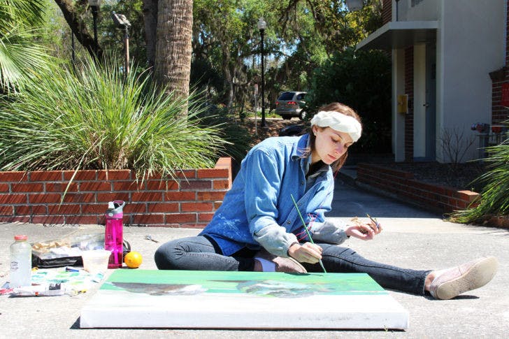 Dayna Lazarowitz, a 20-year-old UF graphic design student, paints a picture of two boulders outside Reid Hall Tuesday afternoon. Lazarowitz was given an assignment to paint outdoors for her art class.