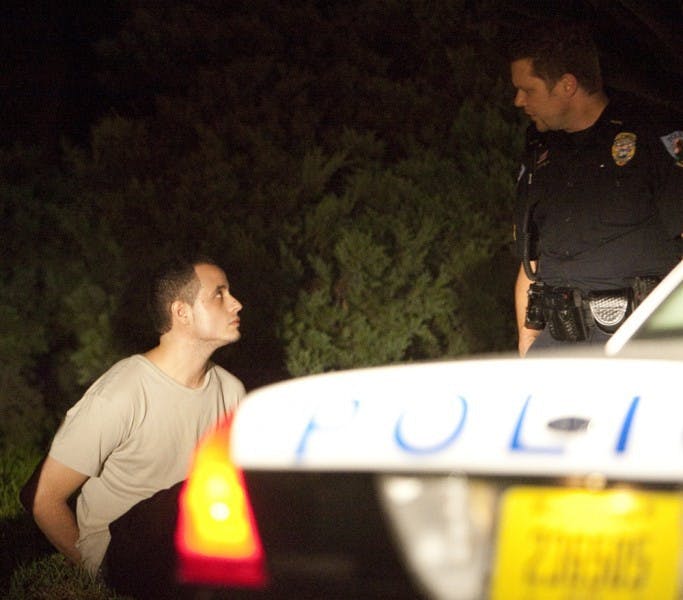Police speak to the driver of a white Lexus sedan carrying suspects in a Thursday morning stabbing on UF's campus.