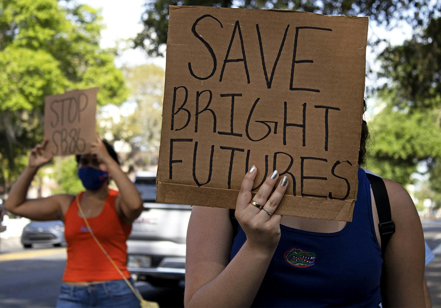 Aleidys Lopez, 19, a UF sustainability studies and women&#x27;s studies sophomore shields her face from the sun with a &quot;Save Bright Futures&quot; sign as she three other protestors march down University Avenue on Friday, March 26, 2021. The protest was held to raise awareness about Senate Bill 86, which was amended on Tuesday.