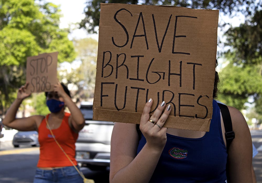 <p>Aleidys Lopez, 19, a UF sustainability studies and women&#x27;s studies sophomore shields her face from the sun with a &quot;Save Bright Futures&quot; sign as she three other protestors march down University Avenue on Friday, March 26, 2021. The protest was held to raise awareness about Senate Bill 86, which was amended on Tuesday.</p>
