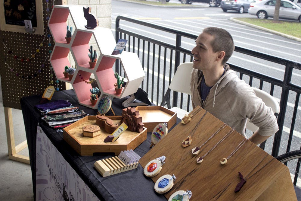 <p>Kyle Jackson, 26-year-old co-owner of Wide Eyed Design, talks to customers at the craft fair outside of Lucky's Market on Saturday. His table was one of several booths as part of the festivities for Lucky's Market One Year Anniversary Celebration.</p>