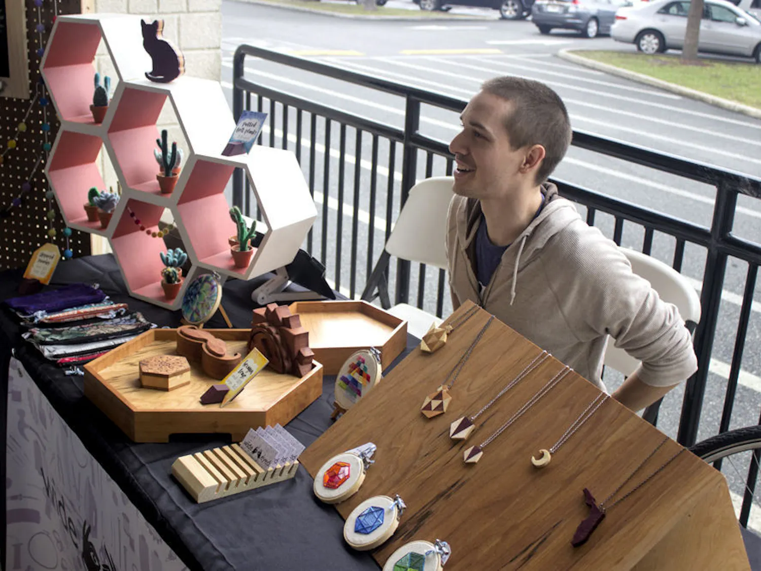 Kyle Jackson, 26-year-old co-owner of Wide Eyed Design, talks to customers at the craft fair outside of Lucky's Market on Saturday. His table was one of several booths as part of the festivities for Lucky's Market One Year Anniversary Celebration.