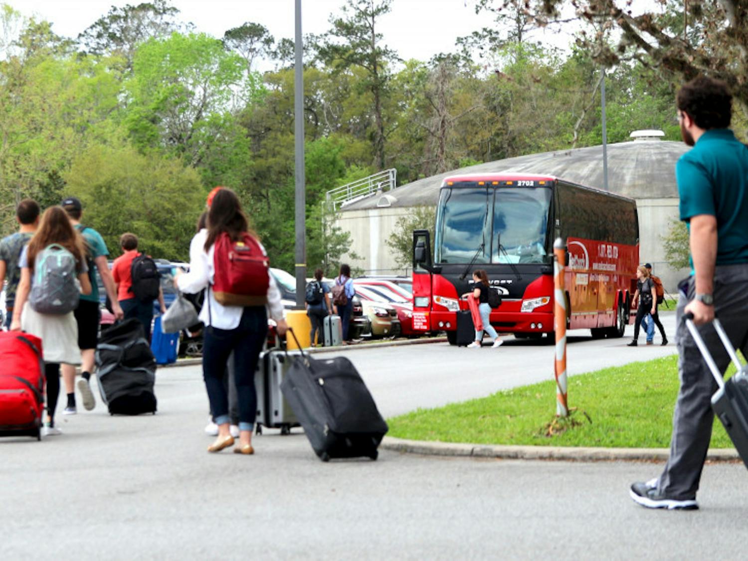 Students and other passengers walk toward a RedCoach bus to begin boarding Thursday afternoon at the Commuter Lot as UF will begin its Spring Break this upcoming week. 