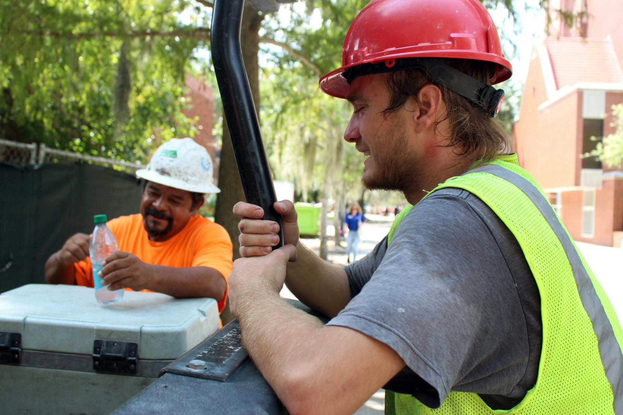 Kyle Markovich (center) cools off in the shade with his co-worker Jjose Llarios (left) in 94-degree heat near Little Hall on Wednesday, August 20, 2025.