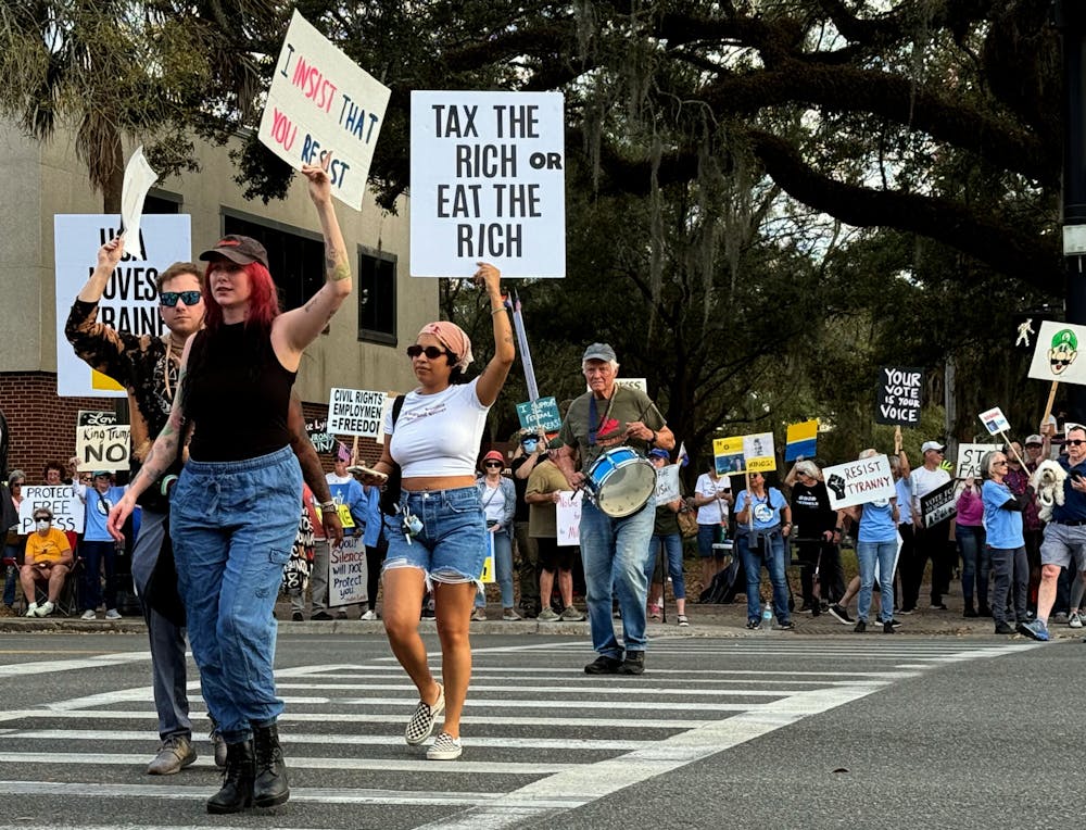 <p>Protesters cross University Avenue holding signs criticizing the Trump administration as a part of the national “March 4th Day of Action" at a demonstration on the Corner of University Ave and Main Street on Tuesday, March 4, 2025.</p>