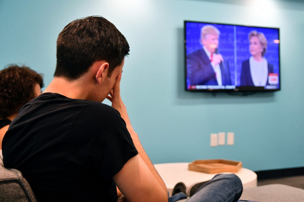 Daniel Hopin, a 20-year-old UF public relations junior, covers his face as he watches the two candidates banter back and forth during the UF College Republicans’ watch party on Sunday evening at Social 28’s south building, located at 311 SW 13th St.