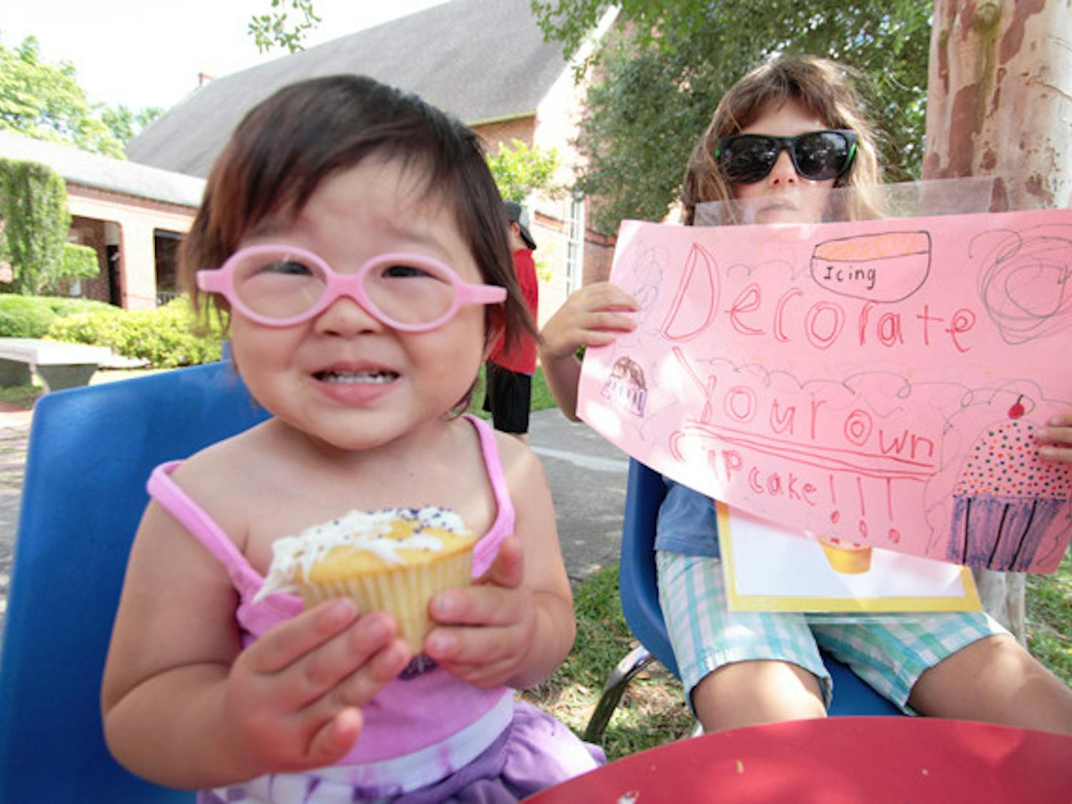 Gainesville resident Mae, 3, shows off a cupcake she iced at the Santa Fe College Spring Arts Festival in 2012 while Jodie, 8, holds a sign promoting the cupcake-decorating to raise money for FUMPers, the preschool of First United Methodist Church.