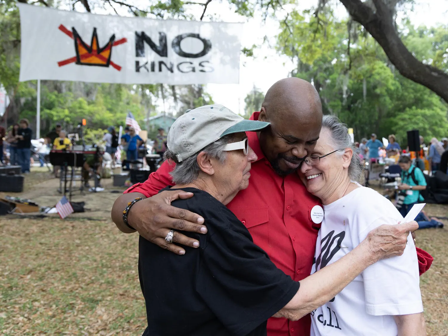 Gary Neal, assistant pastor at New Beginning Christian Worship Center in Micanopy, Fla., embraces two attendants of the No Kings March and Protest at Cora Roberson Park, Saturday, March 28, 2026, in Gainesville, Fla.