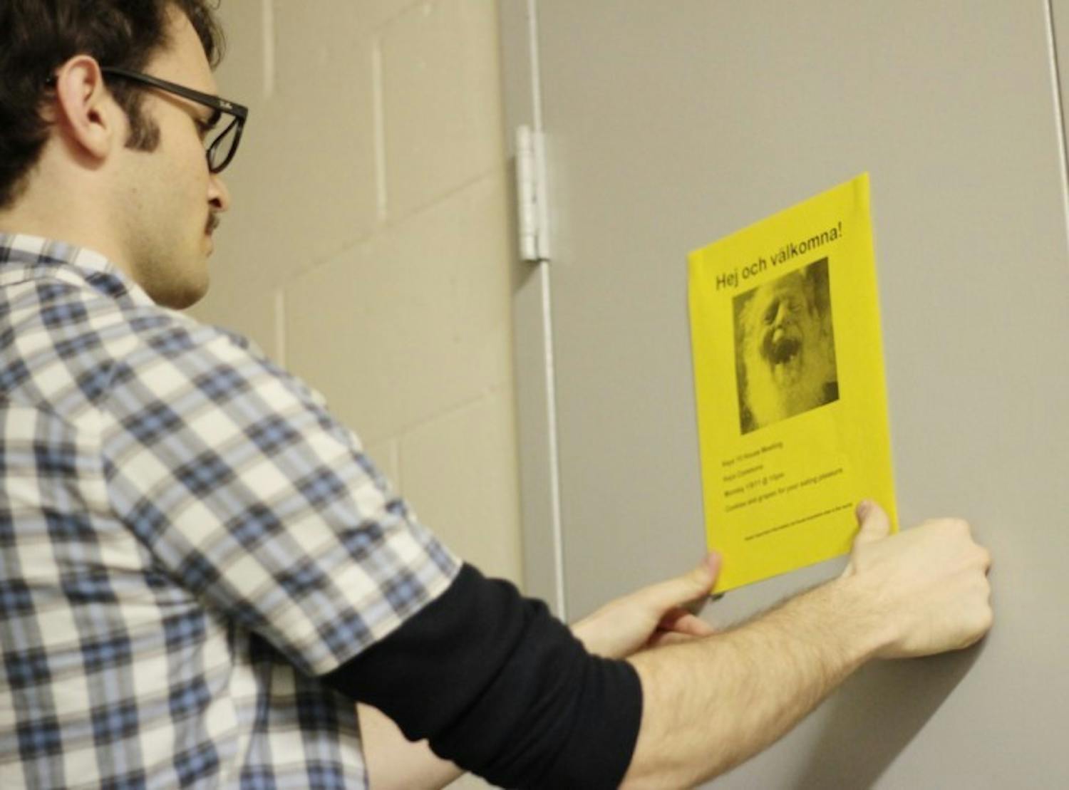 Second-year resident assistant Tyler McCann hangs fliers around his dorm area to alert residents of his spring semester housing meeting.