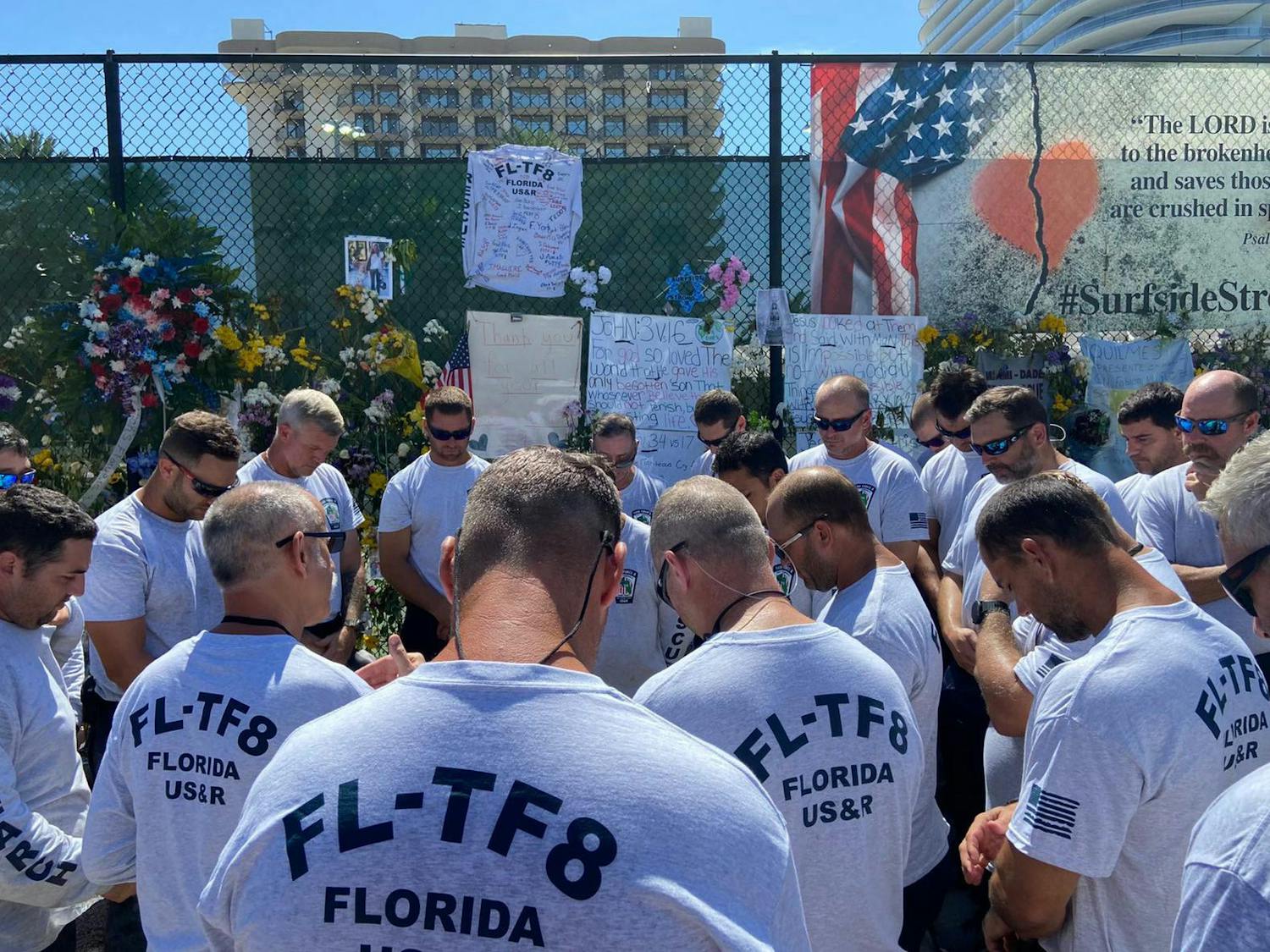 Florida Task Force 8 members bow their heads in front of a memorial wall in Surfside, Florida. Gainesville Fire Rescue sent eight members to Surfside to aid in rescue efforts after the partial collapse of the Champlain Towers South condominium on June 24. 