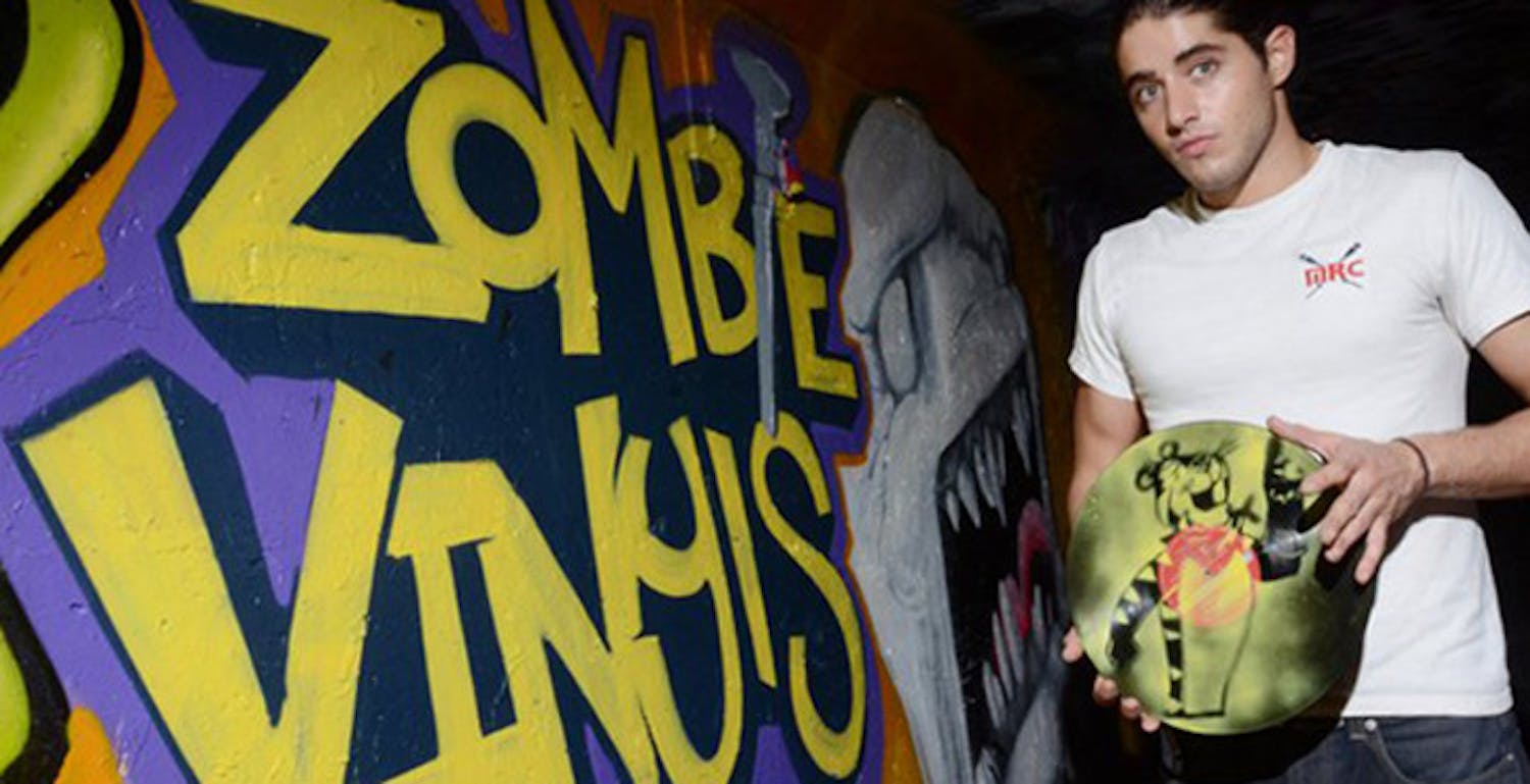 Tony Feria, owner of Zombie Vinyls, poses with a stenciled vinyl in front of a mural painted in the tunnel under 13th Street. Feria began designing art on vinyl about a year ago, when he painted an image of John Lennon on a 12-inch record. He says his inspiration for starting the project came from his love of diverse musical tastes and visual arts. Zombie Vinyls officially became a business in the spring, when Feria's friend and fellow UF graduate Matt Teper pushed Feria to take the project to a higher level.