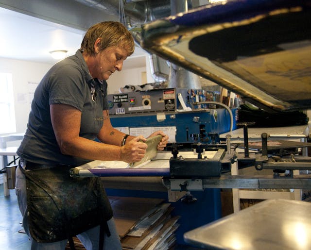 Joy Revels, owner of Dragonfly Graphics, screen-prints a design for a local school. The company makes about 150,000 screen-printed shirts a year.