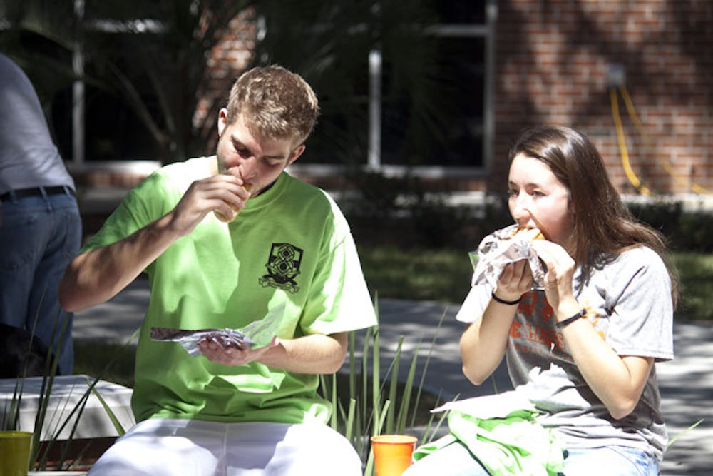 <p>Jonathan Braam, a 19-year-old electrical engineering major, and Torri Cicchirillo, a 19-year-old wildlife ecology major, sit and enjoy a sausage at Murphree Area's eighth annual SausageFest.</p>