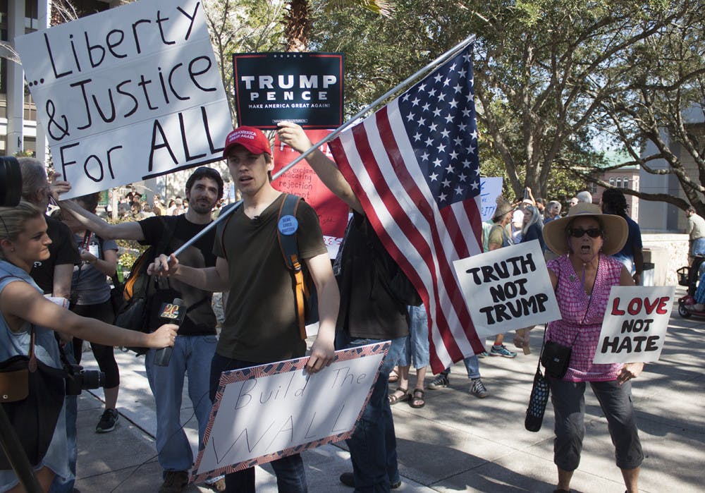 Kevin Lemos, a 19-year-old computer engineering freshman and Trump supporter, talks to the media as Susan Shapiro, an anti-Trump protester, holds anti-Trump signs in front of Gainesville City Hall on Friday, January 20, 2017. “There’s two of them and hundreds of us,” Shapiro said. “We’re here to stand up for our views on inauguration day.”