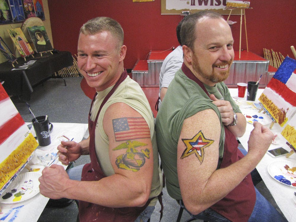 <p class="p1">Marine Corps veteran Jacob Dodd, 29, and Army veteran Greg Revels, 43, pose with their painted tattoos Tuesday afternoon at Painting with a Twist’s Veterans Day event.</p>