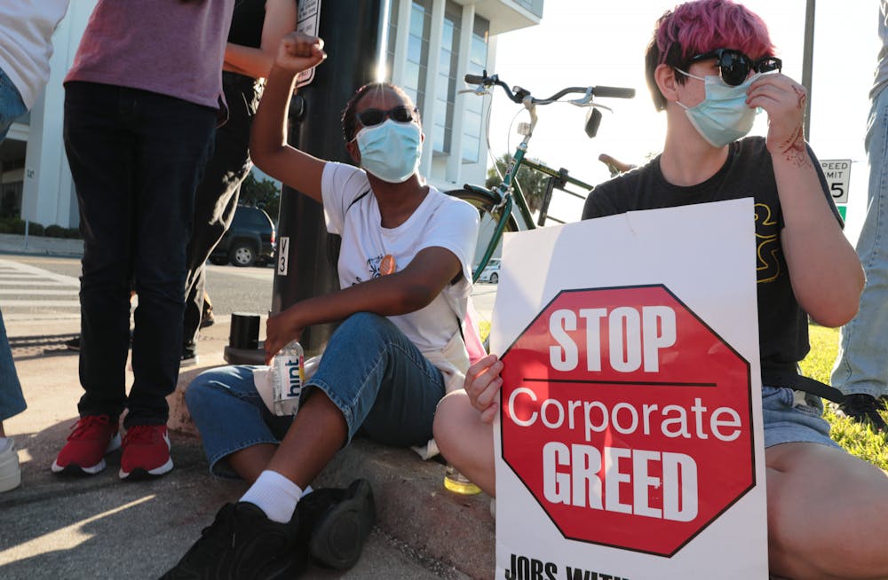 <p>Lea Guthrie (left) and Izzy Myers (right) sit in front of The Collier Companies building during the Protest for Tenant Discrimination on Thursday, Oct. 21, 2021.</p>