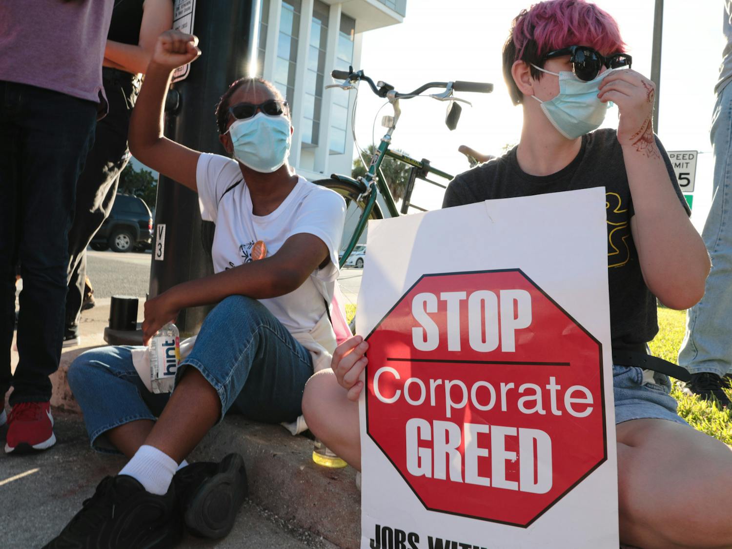 Lea Guthrie (left) and Izzy Myers (right) sit in front of The Collier Companies building during the Protest for Tenant Discrimination on Thursday, Oct. 21, 2021.