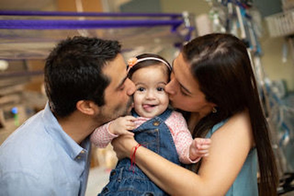 <p>Carlos Ocampo, left, and Victoria Escobar, right, kiss their 1-year-old Valeria Ocampo, who was released from UF Health Shands hospital last Friday.</p>