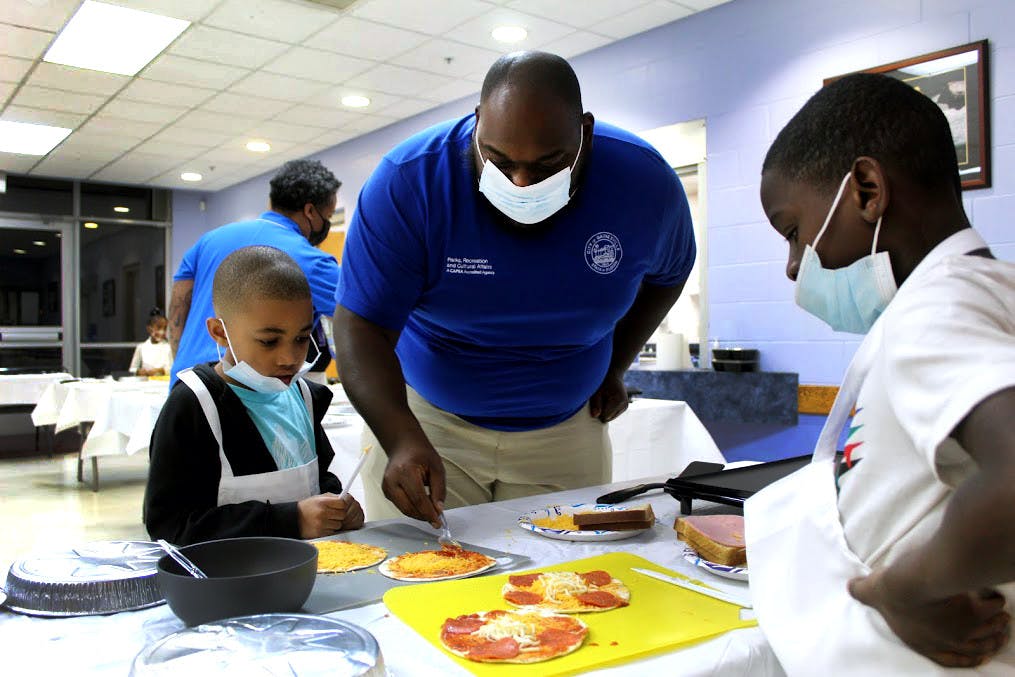Luis McLeod (middle), recreation aide, helps Cayson Dumas (left), 7, and Jacari Holoie (right), 8, grill pepperoni pizzas at the Eastside Community Center on Monday, Jan. 31.