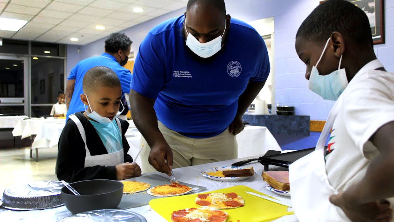 Luis McLeod (middle), recreation aide, helps Cayson Dumas (left), 7, and Jacari Holoie (right), 8, grill pepperoni pizzas at the Eastside Community Center on Monday, Jan. 31.