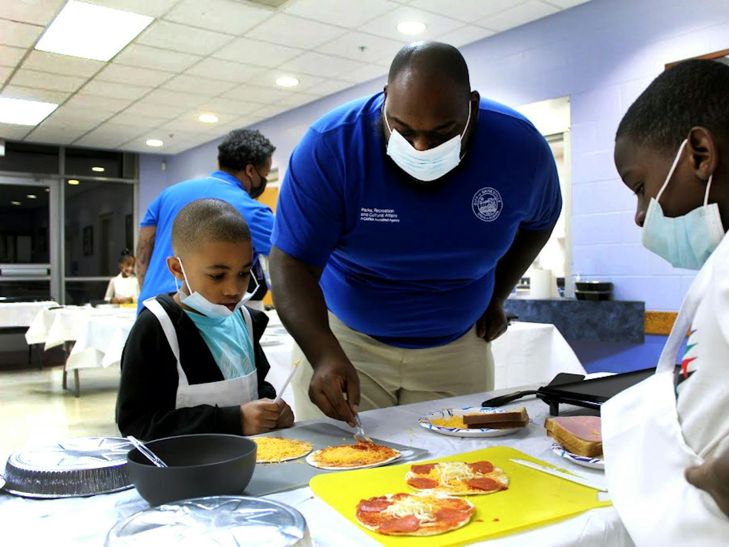 Luis McLeod (middle), recreation aide, helps Cayson Dumas (left), 7, and Jacari Holoie (right), 8, grill pepperoni pizzas at the Eastside Community Center on Monday, Jan. 31.