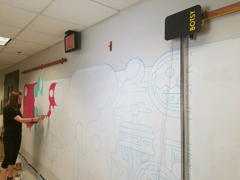 While her robot, Botsy, continues to outline the remaining pieces of a new mural on a once blank hallway in UF’s New Engineering Building, UF alumna Liza Kholodkova begins to paint.