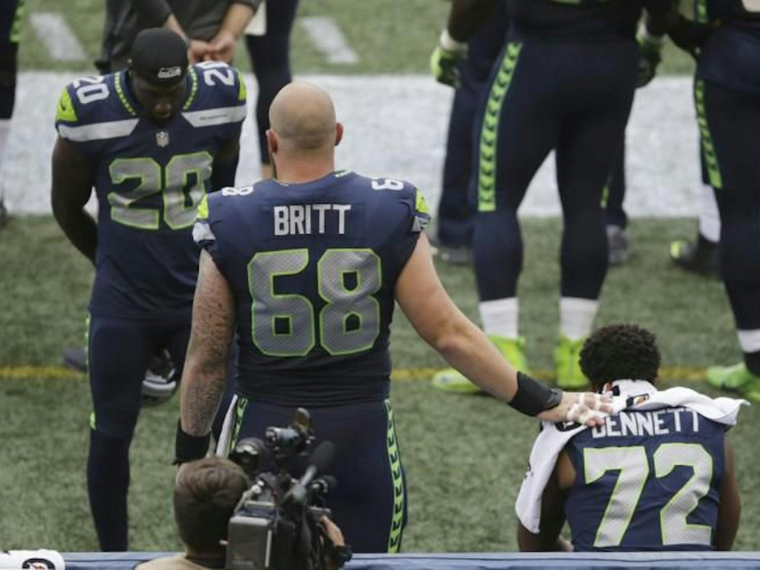 Seahawks center Justin Britt and cornerback Jeremy Lane stand near defensive end Michael Bennett as Bennett sits on the bench during the national anthem Friday, Aug. 18, 2017, in Seattle. (Scott Eklund / AP)