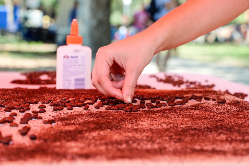 Carley Carbary, a 19-year-old UF religion freshman, places a bean in UF Social Street Team’s community art project (the state of Florida made up of coffee beans) on the Plaza of the Americas on Thursday in honor of National Coffee Day. Limited-edition buttons were given to those who contributed a bean to the project.
