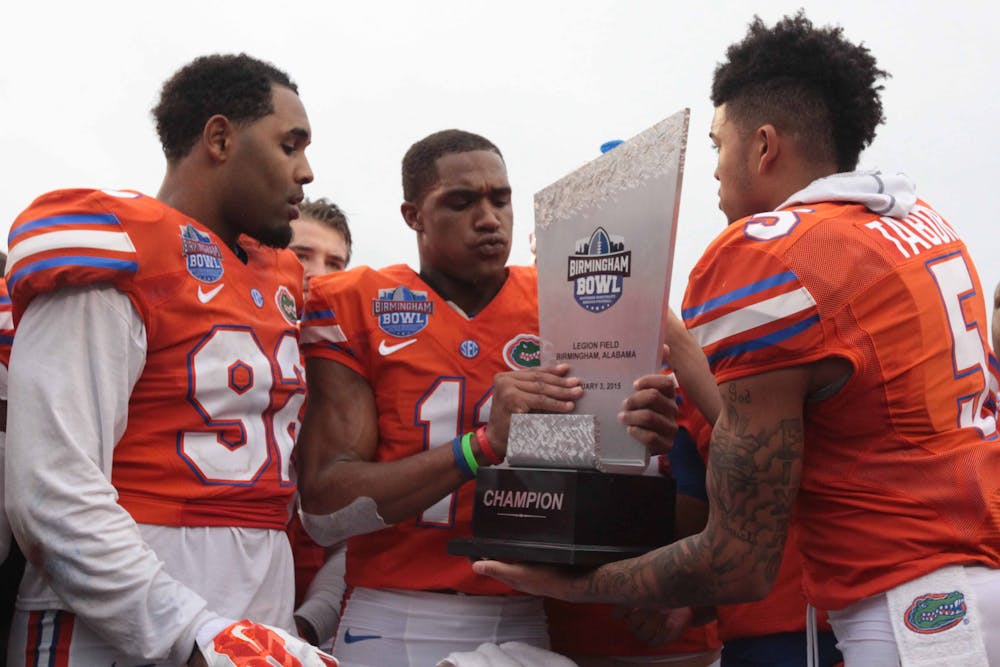 <p>Demarcus Robinson (center) and Jalen Tabor (right) hold the Birmingham Bowl trophy while Gerald Willis looks on</p>