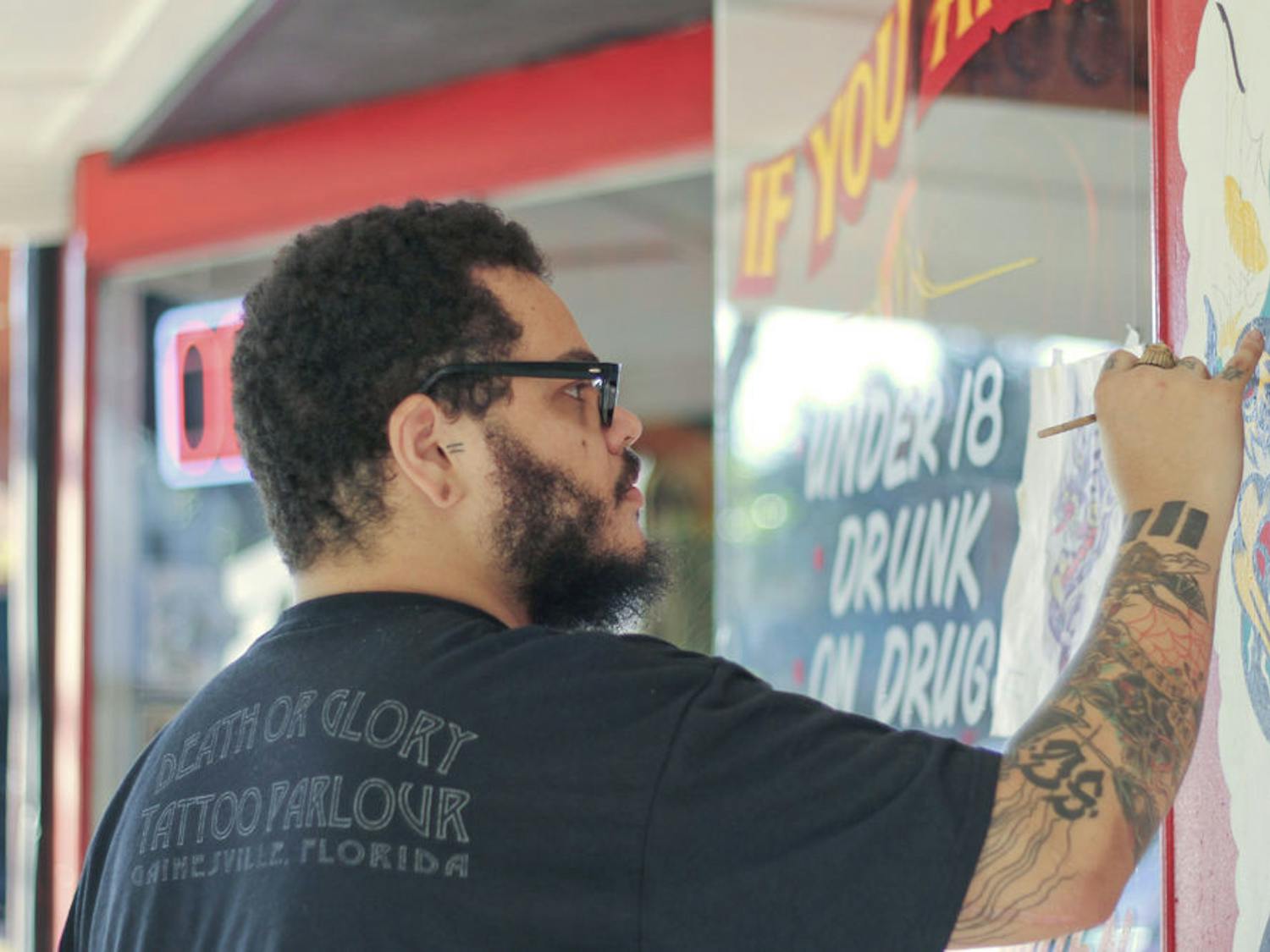 Jesus Lopez, 26, a tattoo artist at Death or Glory Tattoo Parlour, paints a dragon on the face of the shop. The dragon is an old Sailor Jerry design the shop chose to spruce up the building.