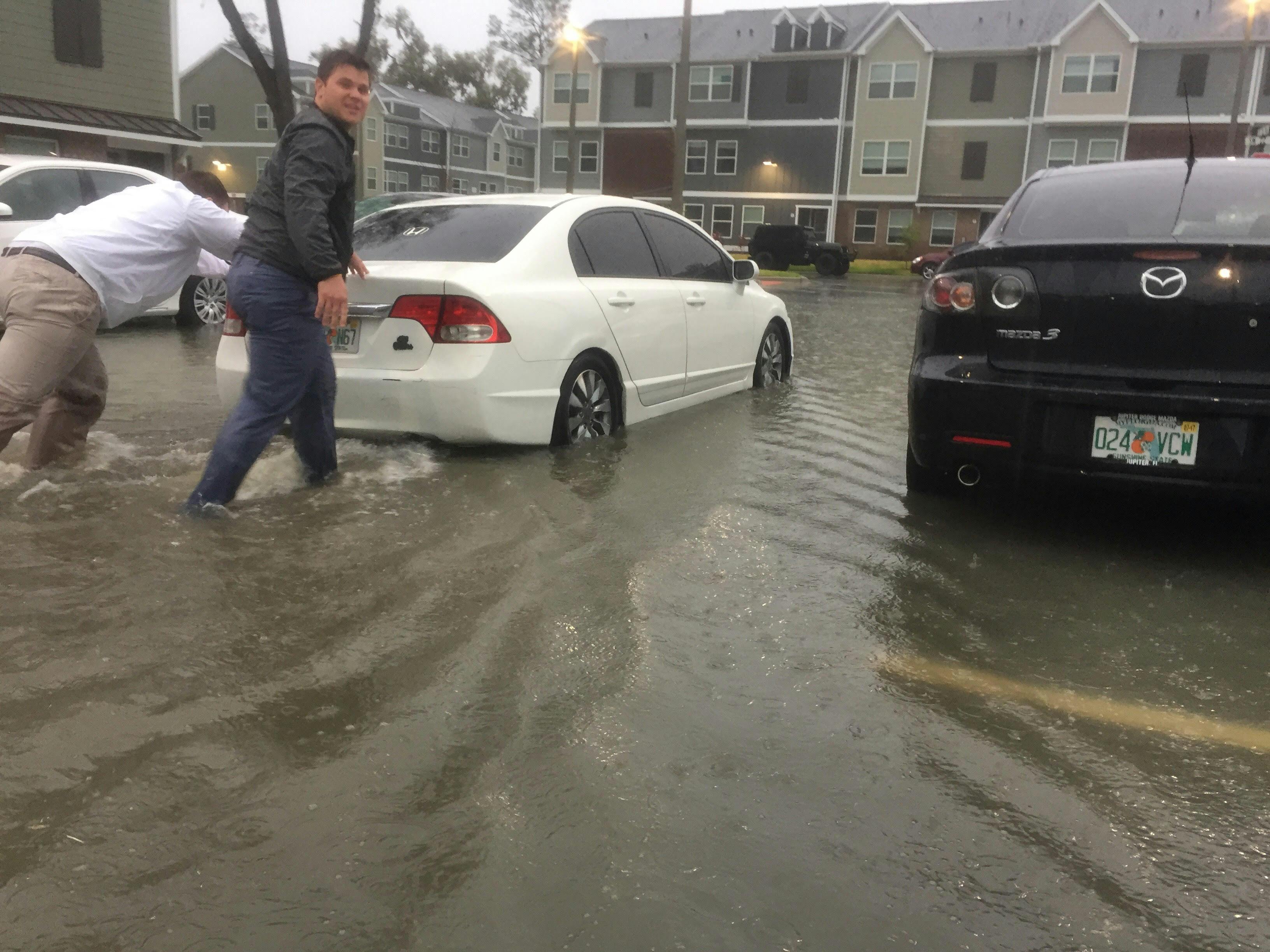 Two men at The Ridge at Gainesville push a car through a flooded parking lot on Tuesday.