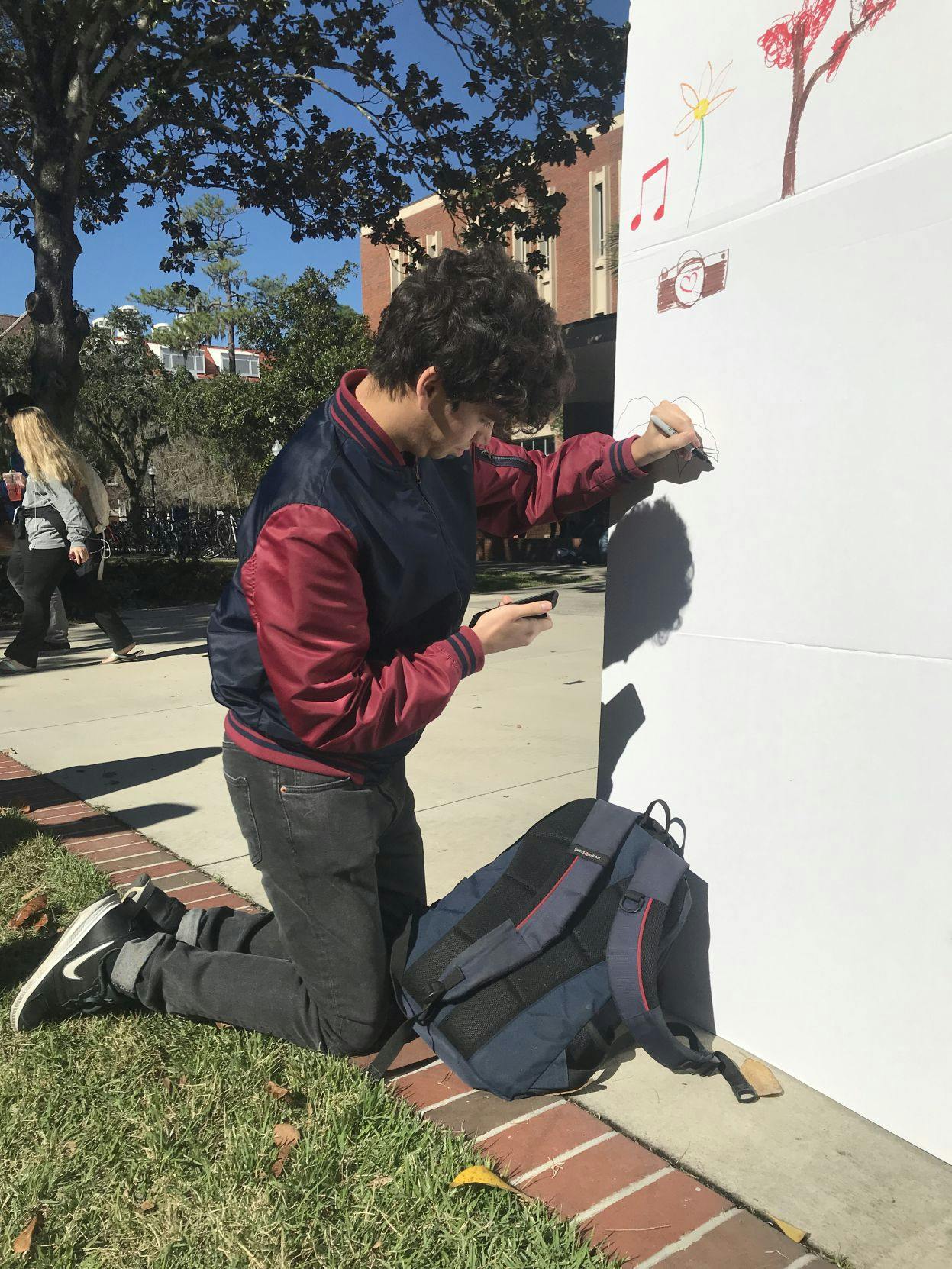 Lev Ettinger, 18, computer science freshman, looks at his phone for reference as he draws popular online meme Pepe the Frog on the “I Am More” wall.&nbsp;