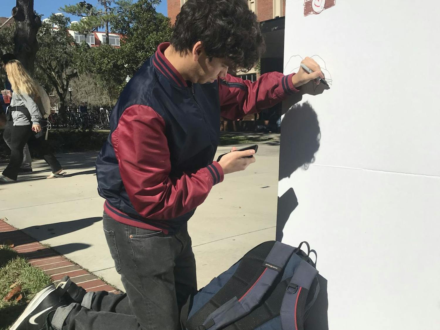 Lev Ettinger, 18, computer science freshman, looks at his phone for reference as he draws popular online meme Pepe the Frog on the “I Am More” wall.&nbsp;