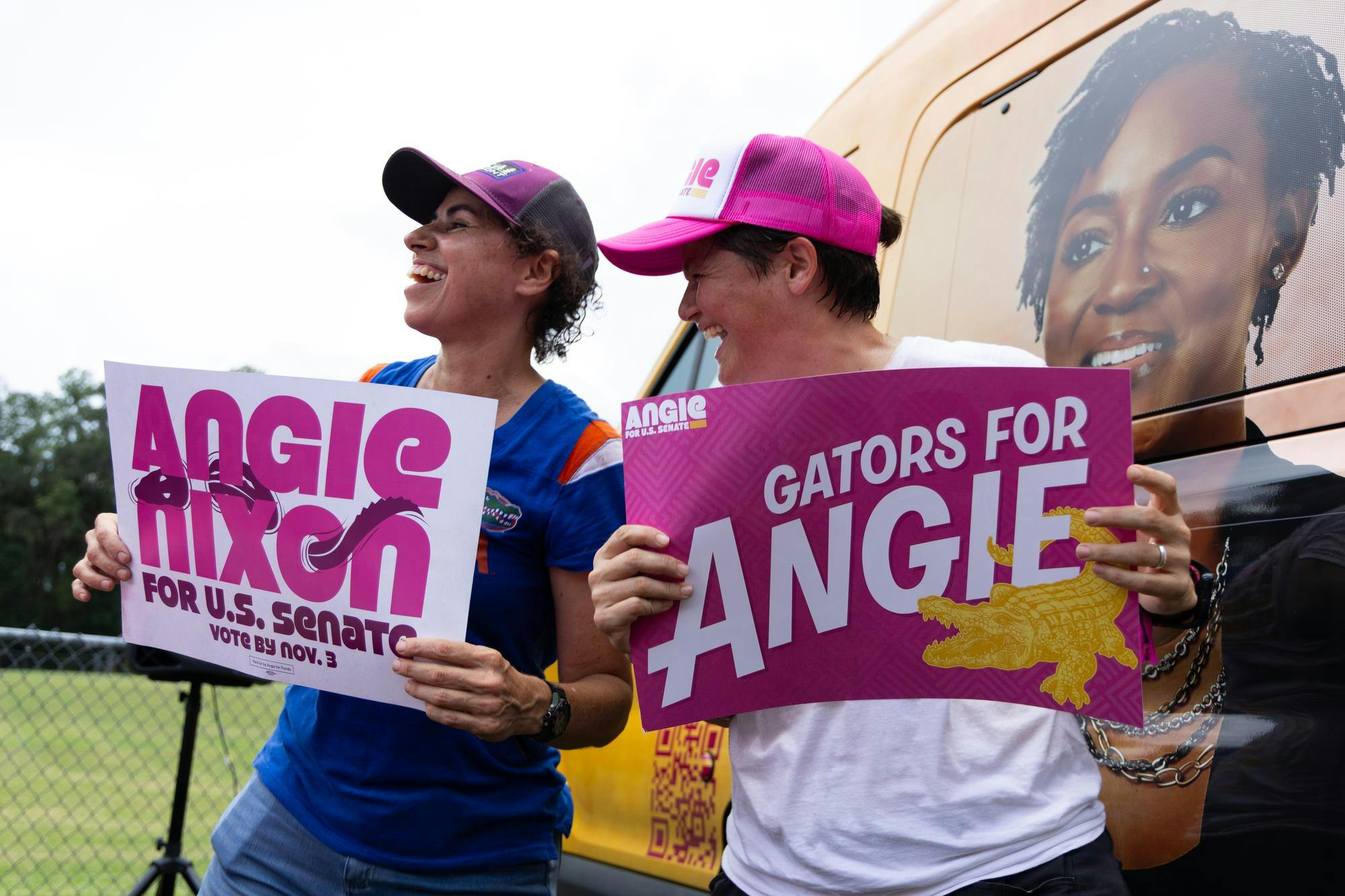 Two supporters of Angie Nixon wave signs in front of the van Nixon rode to the event, Saturday, Sept. 5, 2026, in Gainesville, Fla.
