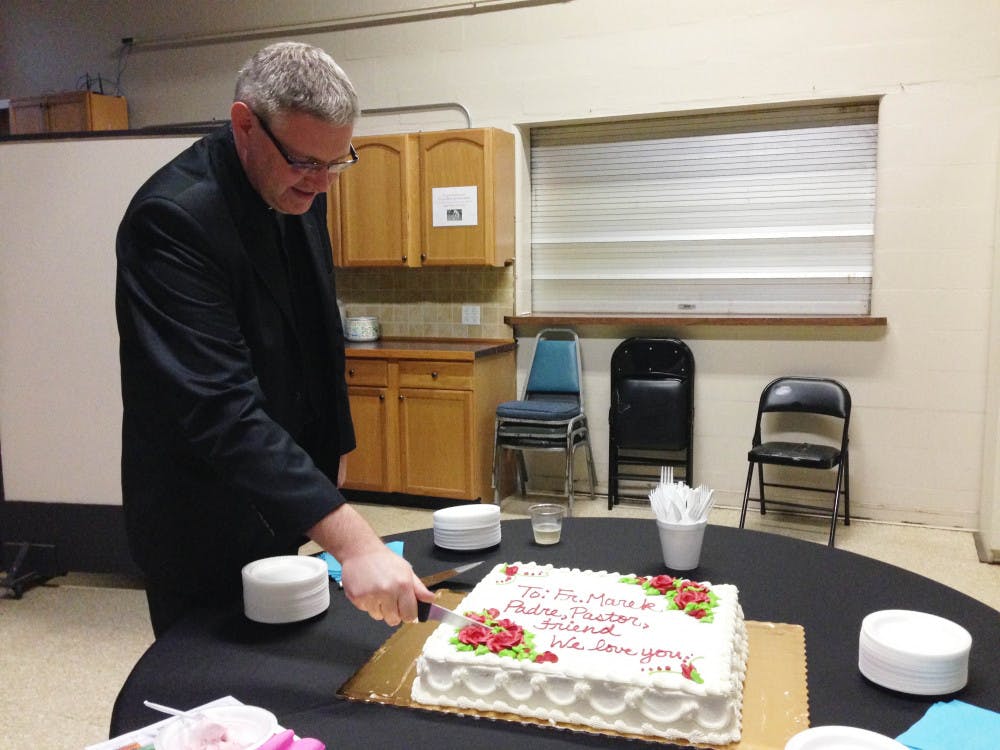 <p>The Rev. Marek Dzien cuts the cake at the celebration for his 20th aniversary as a priest on May 31.</p>