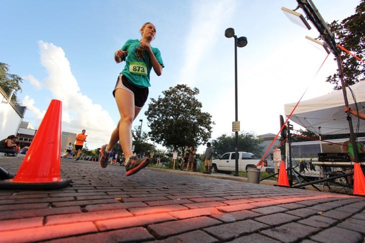 Elizabeth Martin, 26, crosses the finish line during the Gainesville Beer Run 5K race on Friday evening. Runners received free craft beer and and a commemorative mug for participating. Martin finished with a time of 21:02.