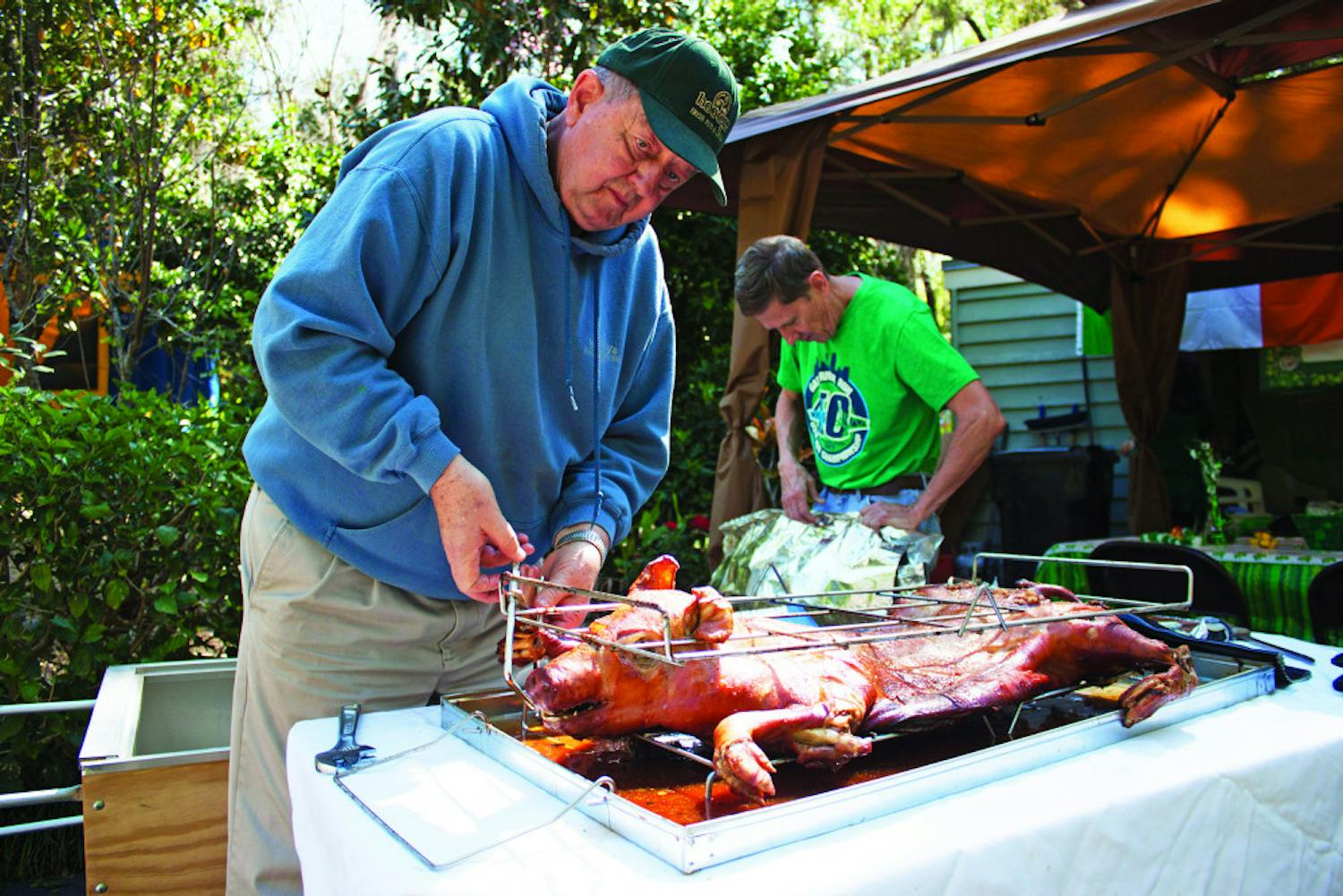 Larry King, 76, loosens a rack holding a roasted pig as Jim Ferrer, 66, makes a tent out of aluminum foil to keep it warm for a day-after-St. Patrick's Day party at the corner of Northwest 14th Avenue and Northwest 18th Street on Saturday. King and Ferrer roasted the pig for about four hours before serving it. 