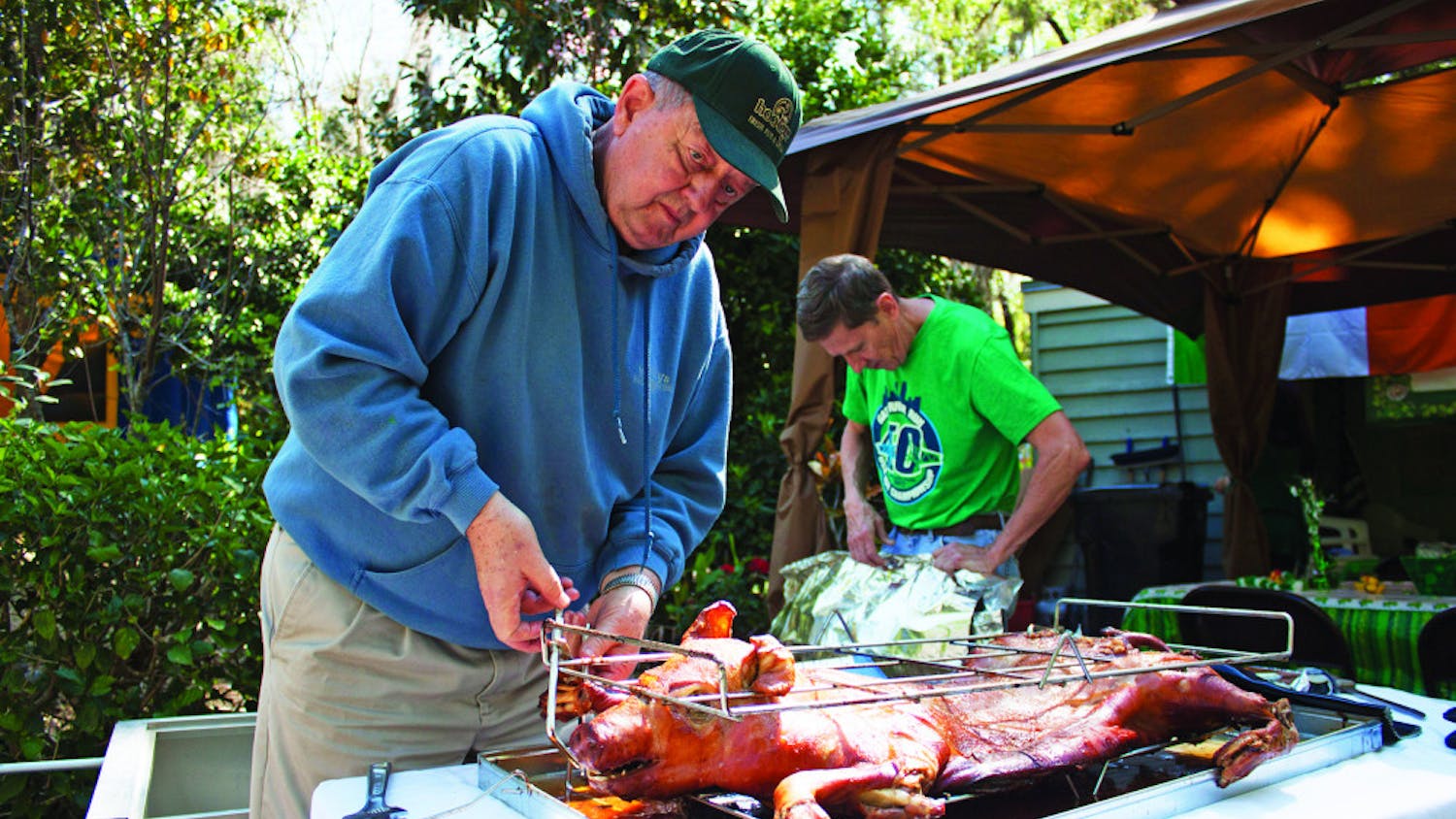 Larry King, 76, loosens a rack holding a roasted pig as Jim Ferrer, 66, makes a tent out of aluminum foil to keep it warm for a day-after-St. Patrick's Day party at the corner of Northwest 14th Avenue and Northwest 18th Street on Saturday. King and Ferrer roasted the pig for about four hours before serving it.