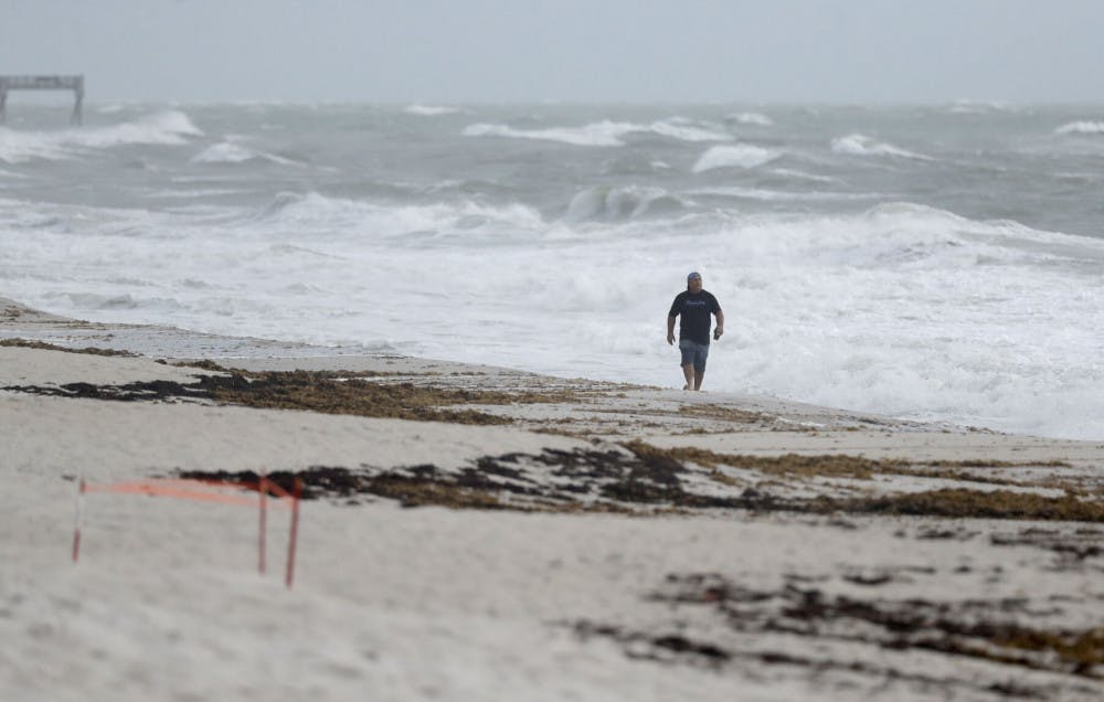 A beach goer walks along the shore as waves churned up by Tropical Storm Isaias crash near Jaycee Beach Park, Sunday, Aug. 2, 2020, in Vero Beach, Fla. Isaias weakened from a hurricane to a tropical storm late Saturday afternoon, but was still expected to bring heavy rain and flooding as it barrels toward Florida. (AP Photo/Wilfredo Lee)
